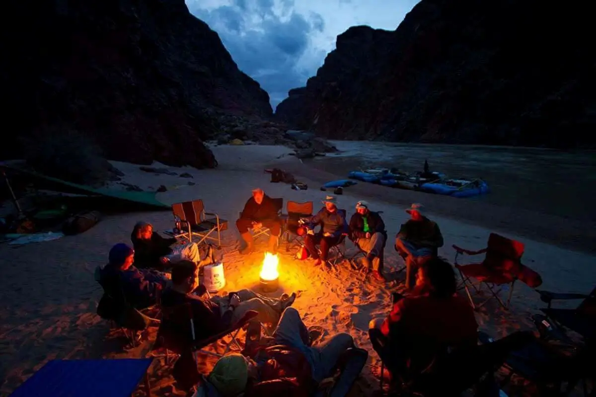Overnight Rafting Multi-day rafters sitting at camp riverside and relaxing by the campfire during an overnight rafting trip in Colorado with Browns Canyon Rafting.