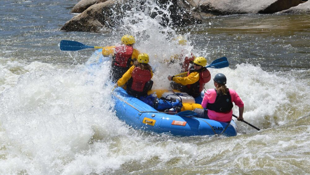 Whitewater raft navigating a churning rapid with paddlers leaning forward into the spray on late season raft trip