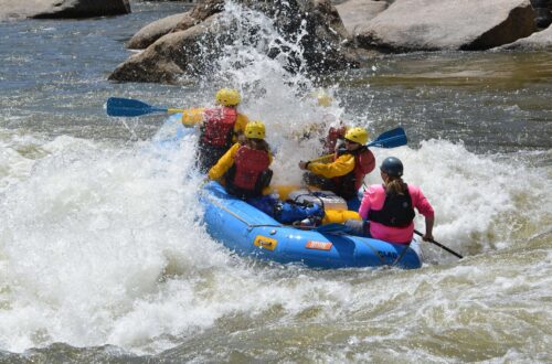 Whitewater raft navigating a churning rapid with paddlers leaning forward into the spray on late season raft trip