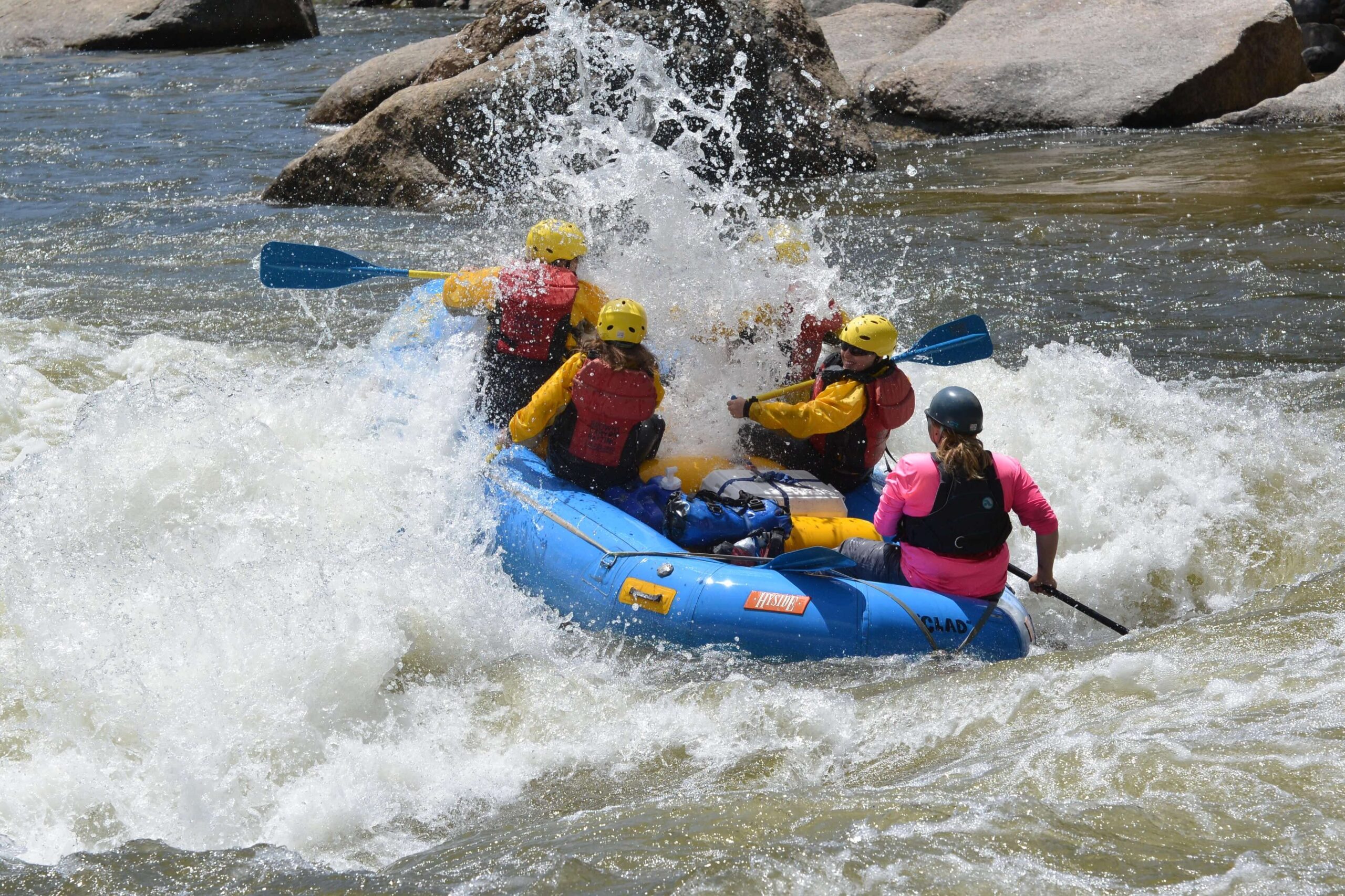 Whitewater raft navigating a churning rapid with paddlers leaning forward into the spray on late season raft trip